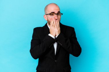 Genç, beyaz, kel bir adam mavi arka planda izole edilmiş. Şok olmuş, ağzı ellerle kaplanmış, yeni bir şey keşfetmeye hevesli..