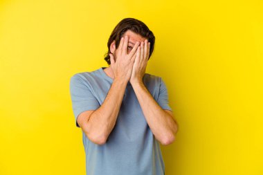 Orta yaşlı, beyaz bir adam sarı arka planda izole edilmiş. Korkmuş ve gergin parmaklarıyla göz kırp..