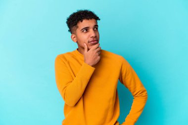Genç Afro-Amerikan kıvırcık adamı şüpheli ve şüpheci bir ifadeyle mavi bir tarafa bakıyor..