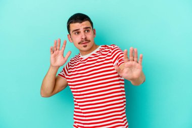 Mavi arka planda izole genç beyaz adam yakın bir tehlike nedeniyle şoka uğruyor