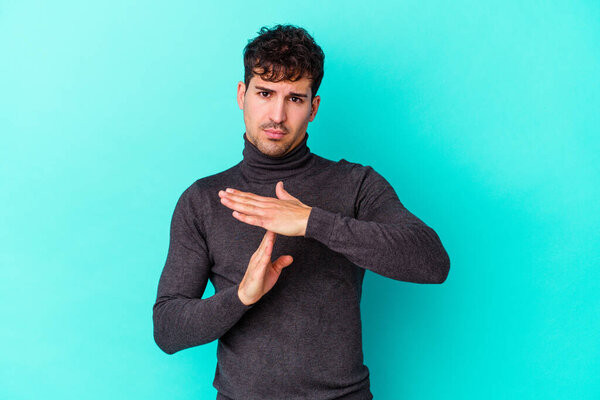 Молодой кавказский мужчина на голубом фоне показывает жест тайм-аута.