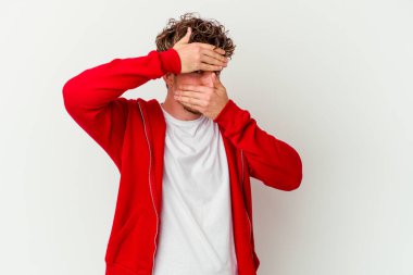 Beyaz arka planda izole edilmiş genç beyaz bir adam kameraya parmaklarıyla göz kırpıyor, yüzünü kapatmaktan utanıyor..