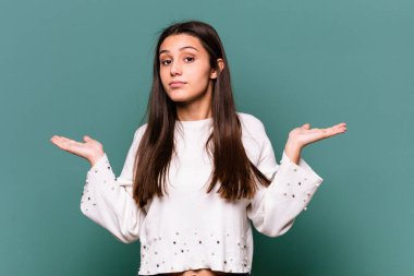 Mavi arka planda izole edilmiş genç bir Hintli kadın. Kafası karışmış ve omuz silkiyor. Kopya alanını tutmak için..