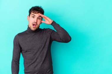 Mavi arka planda izole edilmiş genç beyaz adam yüksek sesle bağırıyor, gözleri açık ve elleri gergin tutuyor..