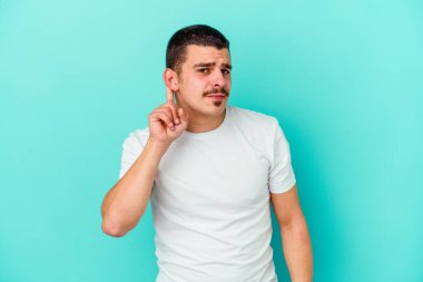 Mavi arka planda izole edilmiş genç beyaz adam bir dedikoduyu dinlemeye çalışıyor..