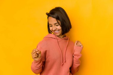 Özel bir günü kutlayan, sarıda izole edilmiş genç İspanyol kadın atlıyor ve enerjiyle kollarını kaldırıyor..