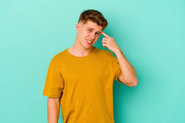 Mavi arka planda izole edilmiş genç beyaz adam işaret parmağıyla bir hayal kırıklığı jesti gösteriyor..