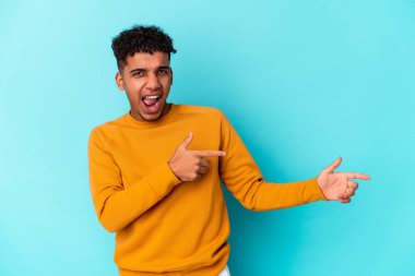 Genç Afro-Amerikan kıvırcık adamı mavi üzerine izole edilmiş, işaret parmağıyla fotokopi çekerek heyecan ve arzusunu ifade ediyor..