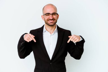 Genç, beyaz, kel bir adam mavi arka planda izole edilmiş. Parmakları aşağıda, olumlu hisler içinde..