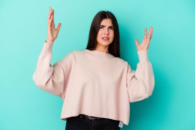 Mavi arka planda izole edilmiş genç beyaz kadın gökyüzüne haykırıyor, yukarı bakıyor, hayal kırıklığına uğramış..