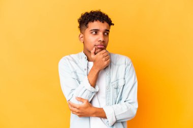 Genç Afro-Amerikan kıvırcık adamı, mor renkte izole edilmiş, kuşkulu ve kuşkulu bir ifadeyle yana bakıyor..