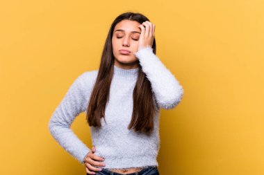 Sarı arka planda izole edilmiş genç Hintli kadın yorgun ve uykulu ellerini başının üstünde tutuyor..