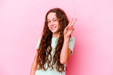 Küçük beyaz kız pembe arka planda izole edilmiş neşeli ve kaygısız parmaklarıyla barış sembolü gösteriyor..