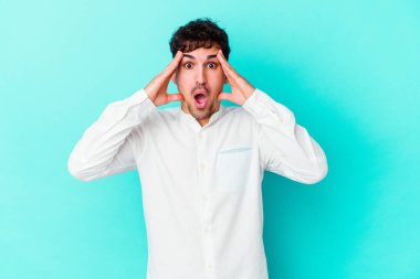 Mavi arka planda izole edilmiş genç beyaz adam yüzünün yarısını palmiye ile kaplayarak eğleniyor..