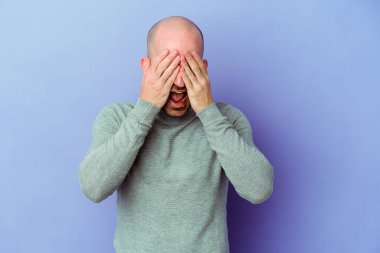 Mor arka planda soyutlanmış beyaz saçlı genç bir adam elleriyle gözlerini kapatıyor, geniş bir gülümsemeyle bir sürpriz bekliyor..