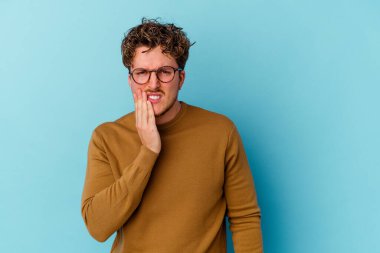 Mavi arka planda izole edilmiş gözlüklü genç beyaz adam güçlü bir diş ağrısı, azıdişi ağrısı var..