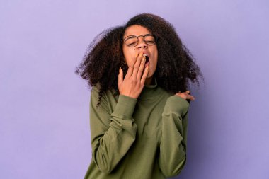 Genç Afro-Amerikalı kıvırcık kadın mor arka planda izole edilmiş esniyor. Ağzını eliyle kapatan yorgun bir hareket sergiliyor..