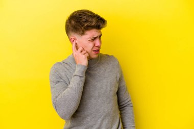 Sarı arka planda izole edilmiş genç beyaz adam elleriyle kulakları örtüyor..