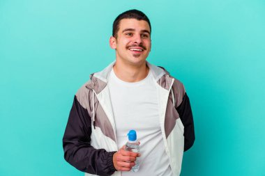 Genç beyaz adam mavi arka planda izole edilmiş su içiyor. Amaçlarına ve amaçlarına ulaşma hayalleri kuruyor.