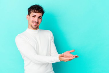 Mavi arka planda izole edilmiş genç beyaz bir adam palmiyesinde bir kopya alanı tutuyor..