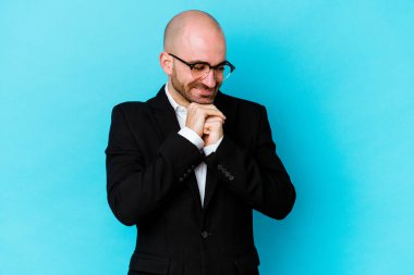 Mavi arka planda izole genç beyaz adam ellerini çenesinin altında tutuyor, mutlu bir şekilde yana bakıyor..