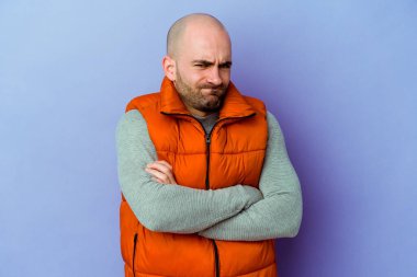 Mor arka planda izole edilmiş beyaz kel bir adam yanakları patlatır, yorgun bir ifadeye sahiptir. Yüz ifadesi kavramı.