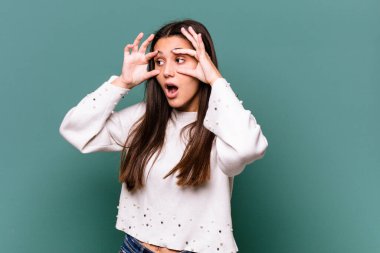 Mavi arka planda izole edilmiş genç Hintli kadın bir başarı fırsatı bulmak için gözlerini açık tutuyor..