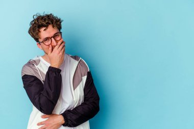 Mavi arka planda izole edilmiş gözlüklü genç beyaz adam gülüyor, kaygısız, doğal duygu..