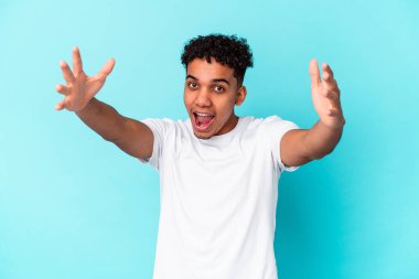 Genç Afro-Amerikalı kıvırcık adam mavi üzerine izole edilmiş zaferi ya da başarıyı kutluyor, şaşırıyor ve şok oluyor..
