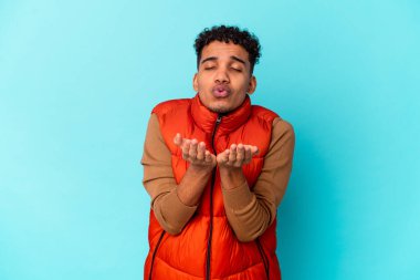 Genç Afro-Amerikan kıvırcık adamı mavi kıvrımlı dudaklarda izole edilmiş ve hava öpücüğü göndermek için avuç içleri tutuyor..