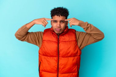 Genç Afro-Amerikan kıvırcık adamı mavi üzerine izole edilmiş bir vazifeye odaklanmış, işaret parmaklarını işaret ediyor..