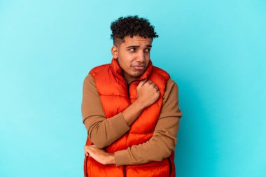 Genç Afro-Amerikalı kıvırcık adam mavi üzerine izole edilmiş kafası karışmış, şüpheli ve güvensiz hissediyor..