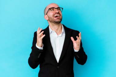 Genç, beyaz, kel bir adam mavi arka planda izole edilmiş. Yüksek sesle gülüyor, elini göğsüne koyuyor..