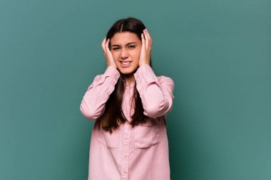 Genç Hintli bir kadın mavi arka planda izole edilmiş kulaklarını elleriyle kapatarak yüksek sesli sesler duymamaya çalışıyor..
