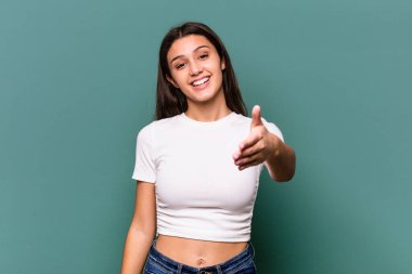 Mavi arka planda izole edilmiş genç Hintli kadın selamlaşma jesti olarak kameraya elini uzatıyor..