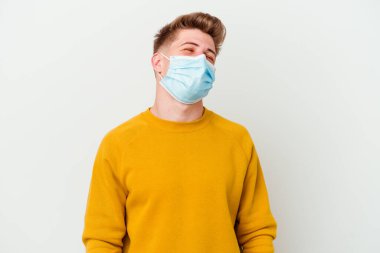 Koronavirüs için maske takan genç adam beyaz arka planda izole edilmiş rahat ve mutlu bir şekilde gülüyor..