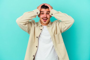 Genç beyaz adam mavi arka planda izole edilmiş bağırıyor, çok heyecanlı, tutkulu, bir şeyden memnun..