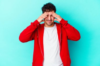 Kafkasyalı genç bir adam mavi arka planda izole edilmiş, başı ağrıyor, yüzüne dokunuyor..