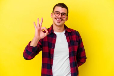 Kafkasyalı genç adam sarı arka planda izole edilmiş neşeli ve kendinden emin iyi bir hareket sergiliyor..