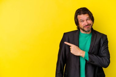 Sarı arka planda izole edilmiş orta yaşlı beyaz bir adam gülümsüyor ve boş alanda bir şeyler gösteriyor..
