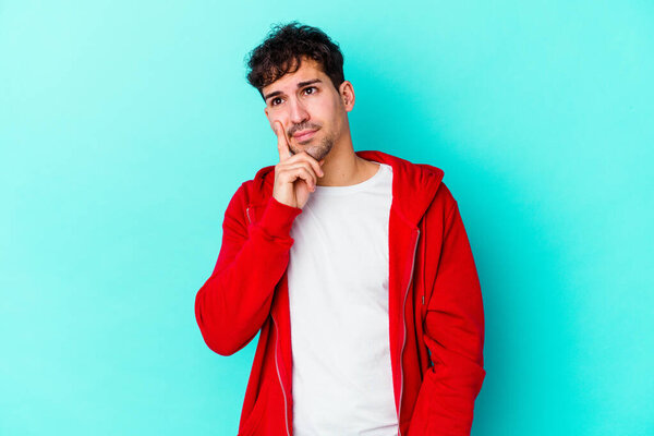 Молодой кавказский человек, изолированный на синем фоне, размышляющий, планирующий стратегию, думающий о бизнесе.