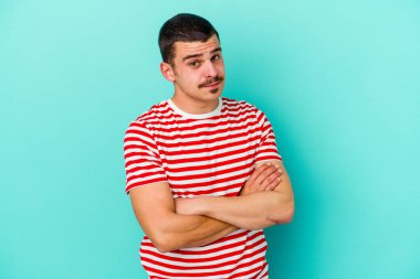 Mavi arka planda izole edilmiş genç beyaz adam alaycı bir ifadeyle kameraya bakarken mutsuz oluyor..