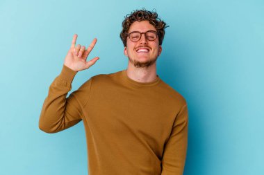 Mavi arka planda gözlük takan genç beyaz bir adam devrim konsepti olarak boynuzlarını gösteriyor..