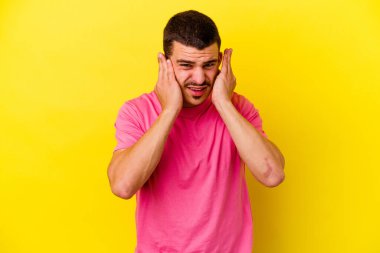 Sarı arka planda izole genç beyaz adam parmaklarıyla kulakları örtüyor, stresli ve umutsuz yüksek sesli bir ortam tarafından.