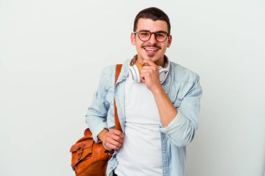 Beyaz arka planda müzik dinleyen beyaz tenli genç bir öğrenci mutlu ve kendinden emin gülümsüyor, elleriyle çenesine dokunuyor..