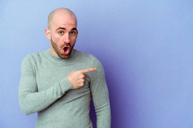 Mor arka planda izole edilmiş beyaz kel bir adam gülümsüyor ve boş alanda bir şeyler gösteriyor..