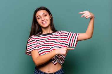 Genç Hintli kadın mavi arka planda izole edilmiş. Elinde küçük bir işaret parmağı olan, gülümseyen ve kendinden emin bir şey tutuyor..