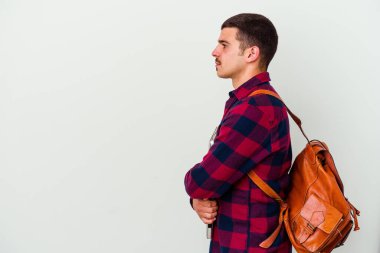 Beyaz arka planda dizüstü bilgisayar tutan beyaz tenli genç bir öğrenci sola bakıyor, yandan poz veriyor.