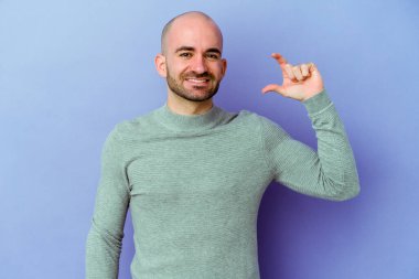 Kafkasyalı genç kel adam mor arka planda izole edilmiş. Elinde parmakları olan, gülümseyen ve kendinden emin bir şey var..