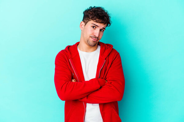 Молодой кавказский человек, изолированный на синем фоне, недовольный взглядом в камеру с саркастическим выражением лица.